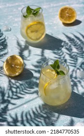 Homemade lemonade with lemon, mint and ice cubes in glasses on a light blue background. Cold summer refreshing drinks. Photo of lemonade with hard shadows. - Shutterstock ID 2184770535