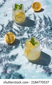 Homemade lemonade with lemon, mint and ice cubes in glasses on a light blue background. Cold summer refreshing drinks. Photo of lemonade with hard shadows. - Shutterstock ID 2184770537