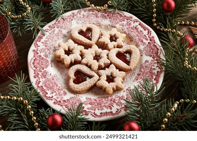 Homemade Linzer Christmas cookies filled with strawberry jam and dusted with sugar on a vintage plate with decorated spruce tree branches - Powered by Shutterstock