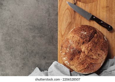 Homemade loaf of artisan sourdough bread on a cutting board next to a knife on a gray concrete background. View of reconciliation with space for text - Powered by Shutterstock