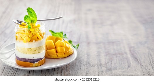 Homemade Mango Dessert, Cheesecake, Trifle, Mouse In A Glass Jar With Spoon On A Light Grey Wooden Background, With Copy Space 