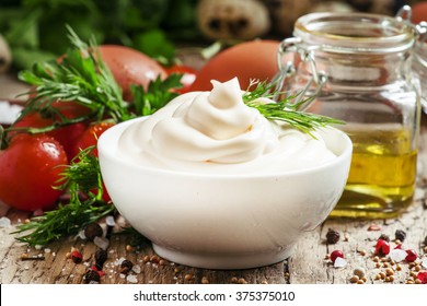 Homemade mayonnaise sauce in a white bowl, jar with olive oil, eggs, salt, spices, mustard, herbs, cherry tomatoes on old wooden background, selective focus - Powered by Shutterstock