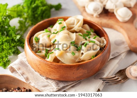 Homemade meat dumplings with onions and parsley- russian pelmeni in wooden bowl.