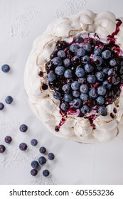 Homemade meringue cake Pavlova with whipped cream, fresh blueberries and blueberry sauce on vintage cake stand on white concrete texture background