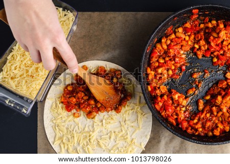 Homemade Mexican food. Making of quesadilla, a woman spreads a stuffing from a frying pan on a tortilla, sprinkled with cheese