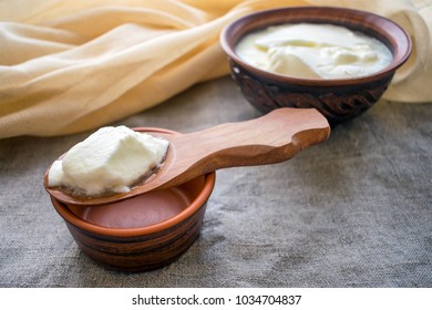 Homemade Milk Yoghurt On A Wooden Spoon Above A Clay Bowl Of Yoghurt. Organic Probiotic Greek Yogurt On Rustic Background. Natural Fermented Milk Diet Drink. Sauce, Tzatziki, Dip