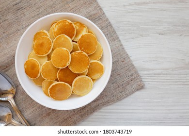 Homemade Mini Pancakes Cereal In A White Bowl On A White Wooden Surface, Top View. Flat Lay, Overhead, From Above. Copy Space.