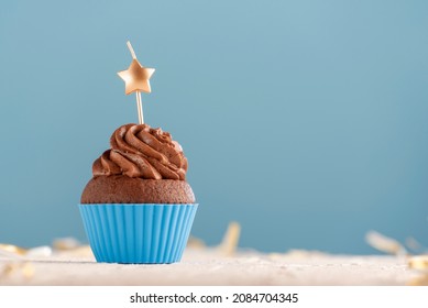 Homemade muffins with chocolate buttercream frosting with candle in the shape of star on blue background