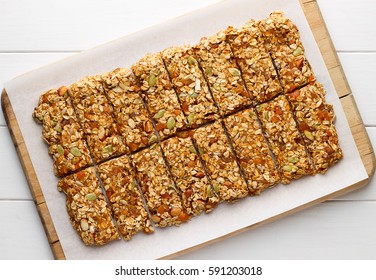 Homemade no bake granola bars with oat flakes, honey, dried apricots and seeds on white baking paper. Healthy energy cereal snacks on wooden background.