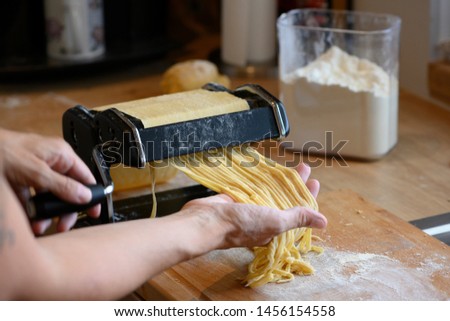 homemade noodles with small manual machine in kitchen with flour
