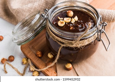 Homemade nutella in a glass jar sprinkled with hazelnuts on a wooden board on a white background - Shutterstock ID 1599452932