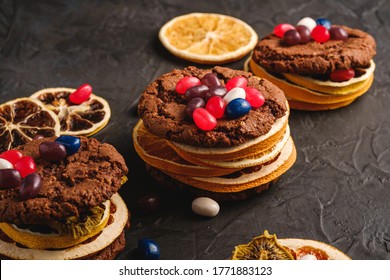 Homemade oat chocolate cookies sandwich with dried citrus fruits and juicy jelly beans on textured dark black background, angle view - Powered by Shutterstock