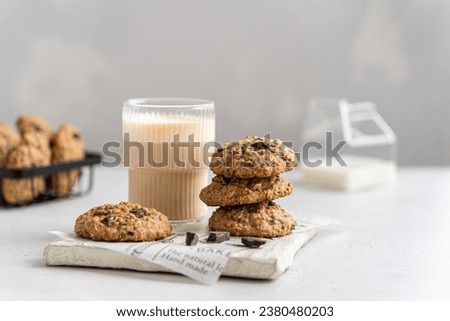 Homemade oatmeal cookies with banana, oats, nuts and chocolate drops on a wooden board with a glass of latte on a light background. Side view, copy space for text. Healthy food. Oatmeat biscuits.