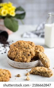 Homemade Oatmeal Cookies With Chocolate Chips In A Small Plate On A Rustic Table. On The Background Of A Flower, Bottles Of Milk, Scattered Chocolate And Cookie Crumbs.