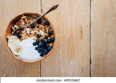 Homemade oatmeal granola with peanuts, blueberry and banana in wooden bowl, sunny morning - Shutterstock ID 499576867