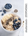 Homemade oatmeal porridge with blueberries, banana and chia seeds in white ceramic bowl, closeup overhead view. Clean eating, dieting and weight loss concept