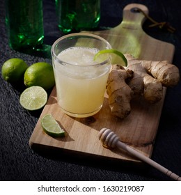 Homemade Organic Ginger Beer With Fresh Limes Serves On A Wood Cutting Board On A Black Woodgrain Table.