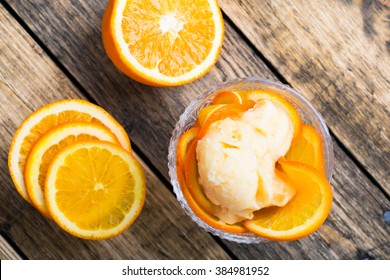 Homemade organic orange ice cream with fresh fruit slices on rustic wooden board, top view