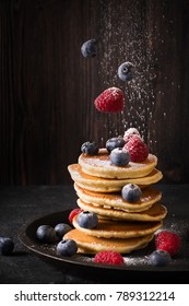 Homemade pancakes stack with sugar, strawberries and blueberries over dark texture. levitation
