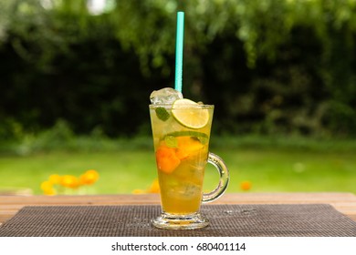Homemade peach ice green tea with lime and lemon balm. On a wooden table outdoors in the garden. Healthy beverages concept.