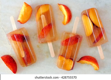 Homemade peach iced tea popsicles with fruit slices on a white marble background