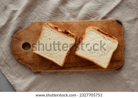 Homemade Peanut Butter and Jelly Sandwich on a rustic wooden board, top view.