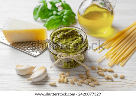 Homemade pesto sauce in small jar and ingredients for pasta on white wooden background with copy space. Traditional Italian cuisine, recipe, restaurant menu
