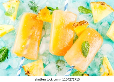 Homemade Pineapple Popsicles on Ice with fresh Pineapple slices and mint, on light blue background copy space top view - Powered by Shutterstock