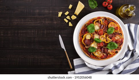 Homemade Pizza With Mozzarella Cheese, Tomatoes, Mushrooms, Salami, Olives, Bell Pepper And Basil On A Platter. Ingredients And Textiles On A Wooden Background. Top View With Copy Space, No People.