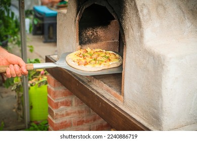 Homemade pizza on a shovel ready to get baked in the outdoor oven - Shutterstock ID 2240886719