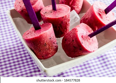 Homemade Popsicles Made With Fresh Blueberries, Raspberries And Yogurt Sitting In A White Bowl On Purple Gingham Napkin