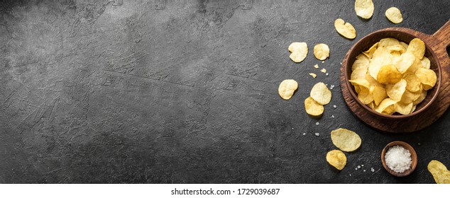 Homemade potato chips in bowl. Crispy potato chips on black background, banner, copy space.