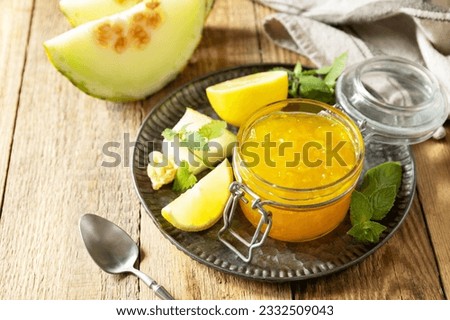 Homemade preserve. Sweet melon and citrus jam or jelly in small glass jar with fresh melon slices on wooden rustic table. Copy space.