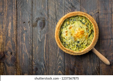 Homemade puff pastry quiche lorraine with leeks swiss gruyere and soft goat cheese with scrumptious golden crust on serving board. Weathered plank barn wood background top view. Copy space