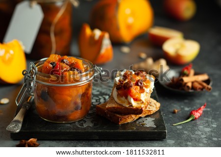 Homemade pumpkin and apple chutney with raisins in jars and on toast bread. Delicious sweet spicy sauce preserved for autumn and winter season.
