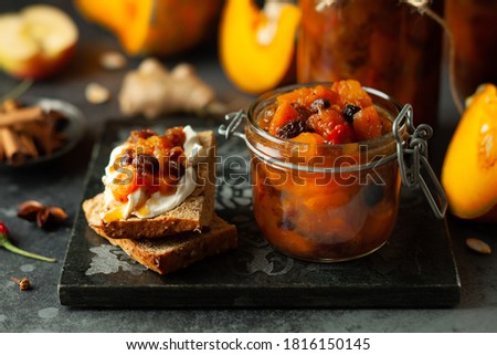 Homemade pumpkin and apple chutney with raisins in jars and on toast bread. Delicious sweet spicy sauce preserved for autumn and winter season.