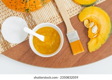 Homemade pumpkin face mask in a small white bowl and make-up brush. Natural autumn beauty treatment and spa recipe. Top view, copy space.  - Powered by Shutterstock