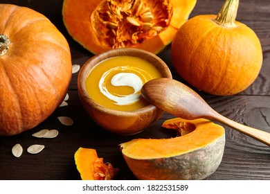 Homemade pumpkin soup with cream and pumpkin seeds in wooden bowl with spoon. Autumn thanksgiving day food concept.
