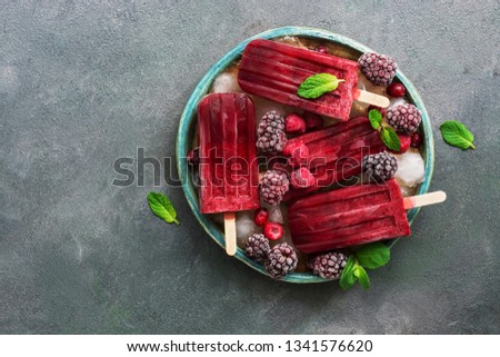 Homemade raspberries blackberry ice cream popsicles decorated berries and mint leaves in plate with ice cubes on gray background.Flat lay, copy space, top view