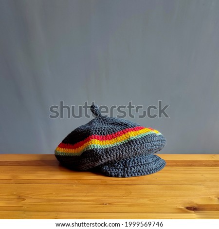 Homemade rasta pattern flat hat with knitting technique with red, yellow and green stripes, placed on a brown wooden table.
