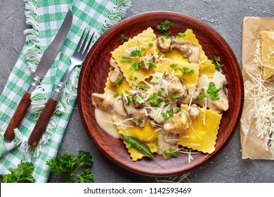 homemade ravioli stuffed with ricotta cheese cooked in creamy garlic mushrooms sauce and served on a plate on a concrete table with napkin and grated parmesan on a paper, close-up