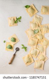 Homemade raw uncooked italian pasta ravioli staffed by spinach ricotta, basil leavrs, pasta cutter. White marble background. Flat lay, space