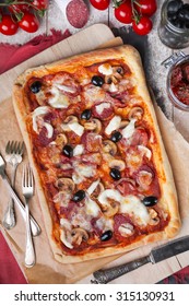 Homemade Rectangular Pepperoni Pizza On A Rustic Table With Ingredients. Photographed From Directly Above.