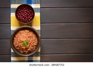 Homemade Red Kidney Bean Spread Garnished With Fresh Coriander Leaf Served In Rustic Bowl, A Bowl Of Raw Kidney Beans Above, Photographed Overhead On Dark Wood With Natural Light