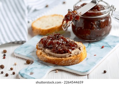 Homemade red onion confit on a slice of bread with liver pate served on a granite serving board, selective focus.