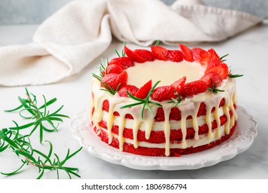 Homemade red velvet cake with white chocolate,  fresh strawberries and rosemary. Delicious gourmet dessert in a white plate on a marble background close-up. Selective focus, copy space