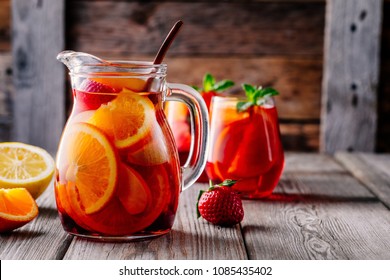 Homemade red wine sangria with orange, apple, strawberry and ice in pitcher  and glass on rustic wooden background