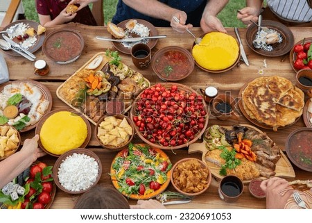 Homemade Romanian Food with grilled meat, polenta and vegetables Platter on camping. 
Top view of group of people having dinner together on wooden table in garden.