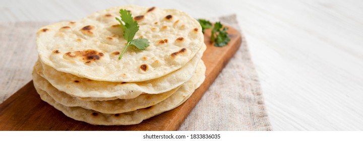 Homemade Roti Chapati Flatbread on a rustic wooden board on a white wooden background, side view. Copy space.