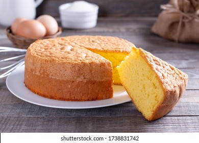 Homemade round sponge cake or chiffon cake on white plate so soft and delicious with ingredients: eggs, flour, milk on wood table. Homemade bakery concept for background and wallpaper.